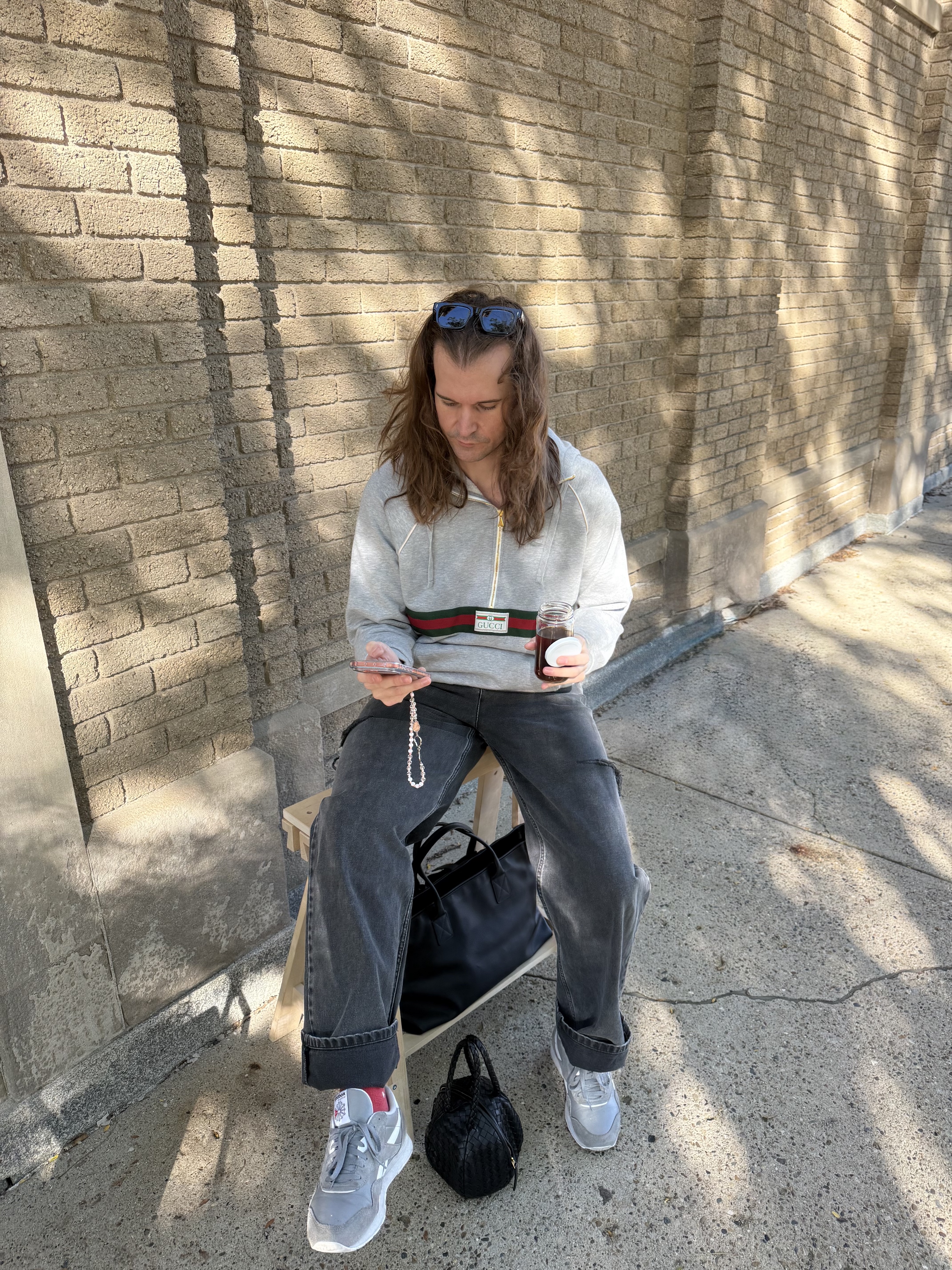 Man seated on the chair, cream sweater, grey trousers, sneakers, phone