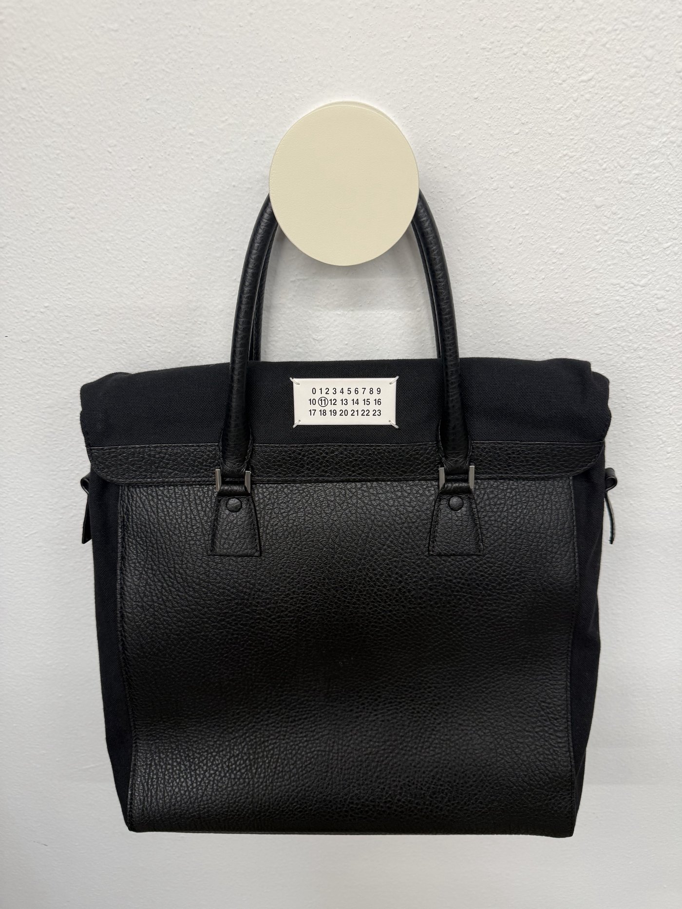 Black Maison Margiela numbered tote bag hanging on a wall hook