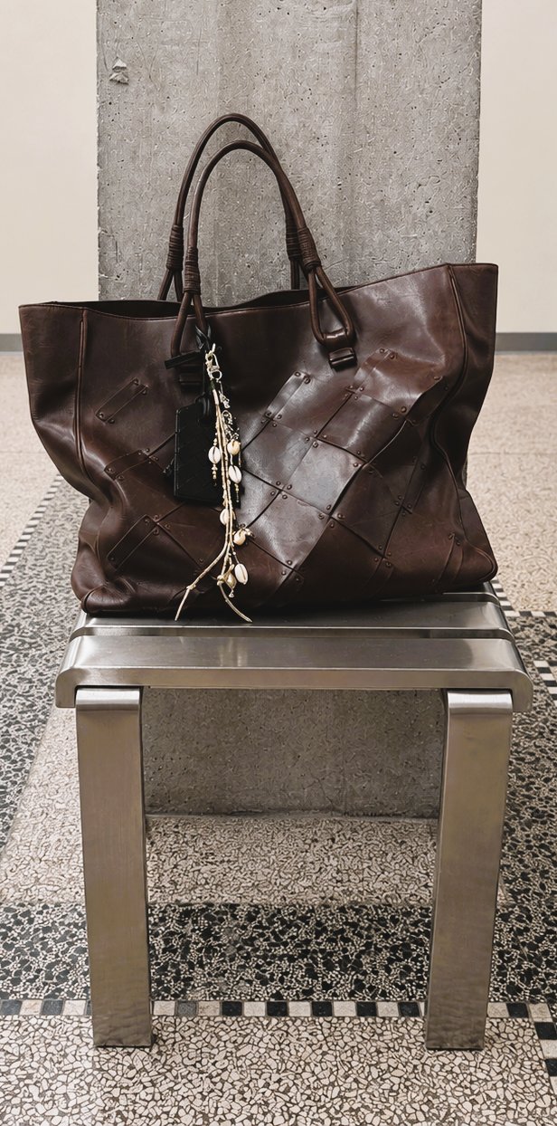 Worn brown leather Bottega Veneta tote bag with a beaded charm on a steel bench
