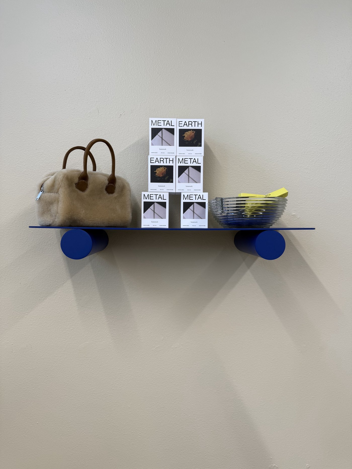 Cobalt blue shelf styled with a shearling bag, Homework fragrance boxes, and a glass bowl