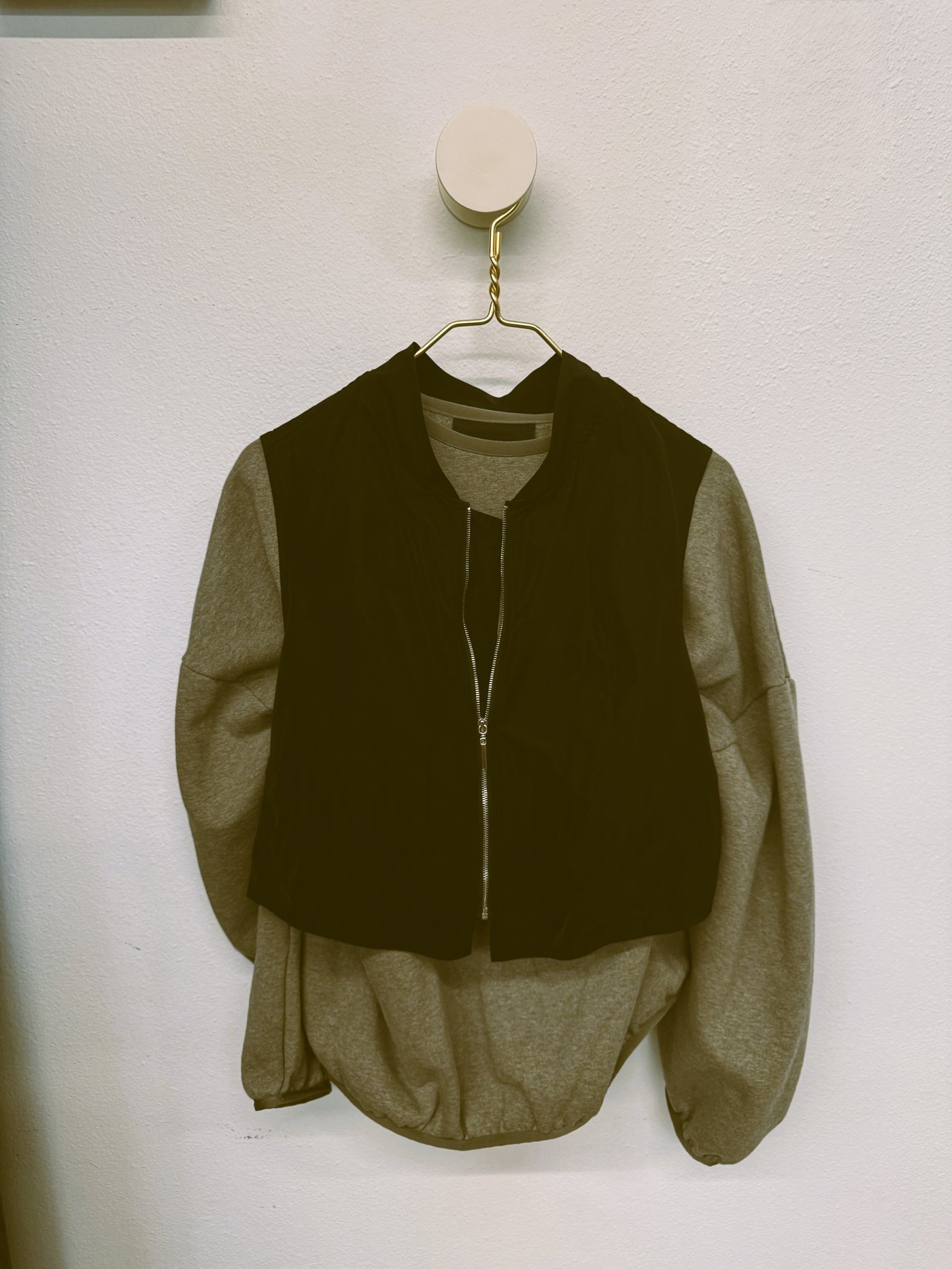 Grey sweatshirt layered under a black zip-up vest on a hanger