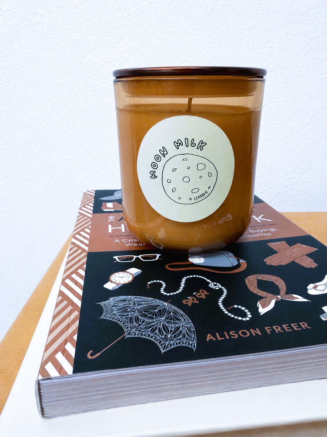 Lemuria Moon Milk candle resting on a stack of books