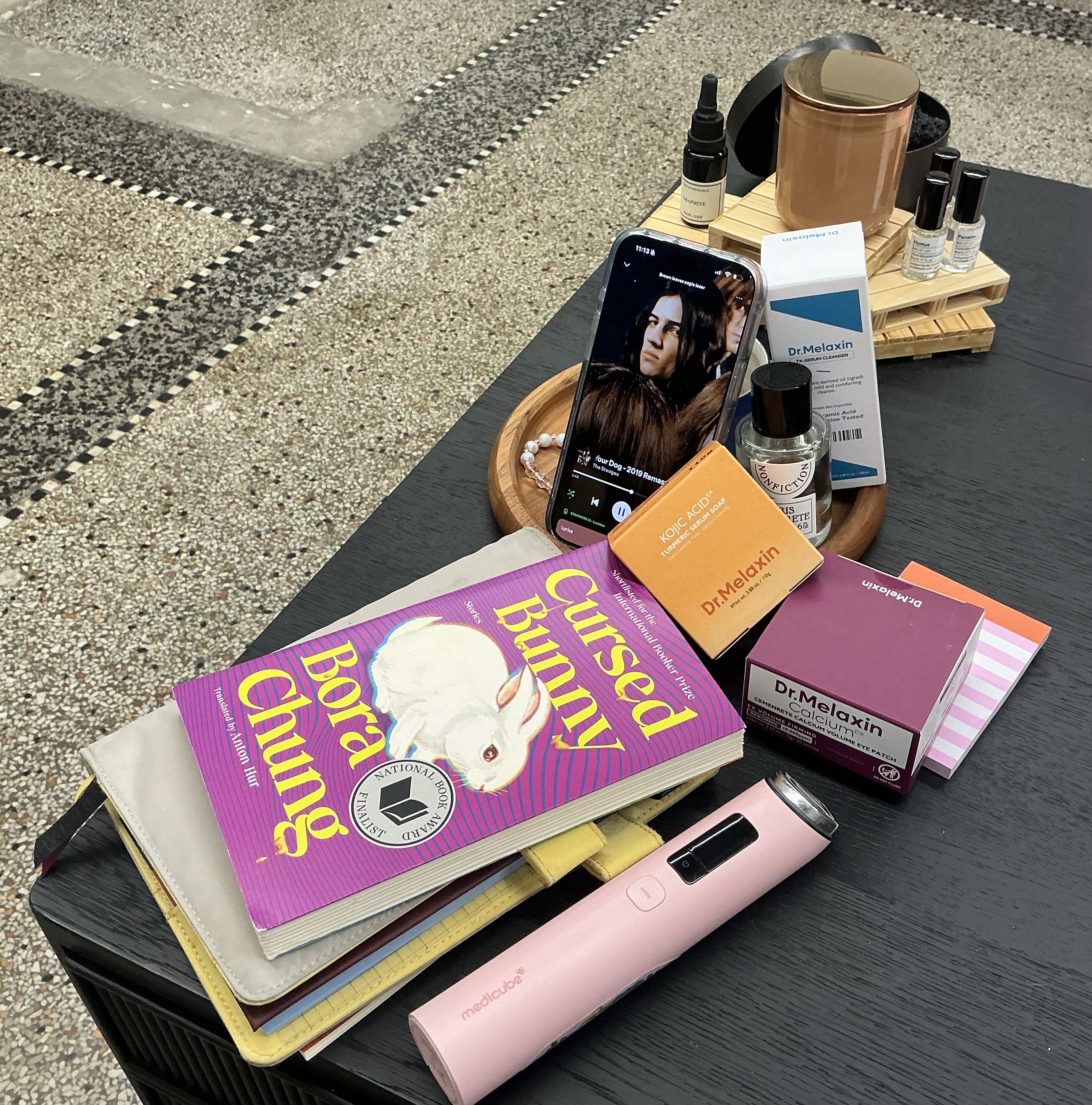 Flat lay: Cursed Bunny book, fragrance, candle, on terrazzo