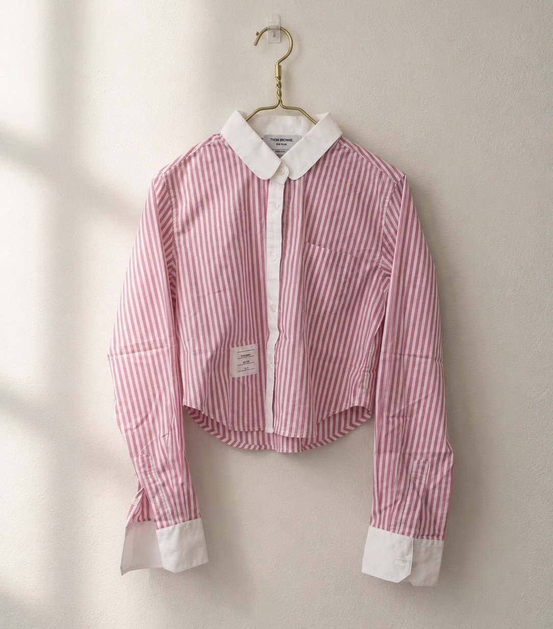 Thom Browne pink and white striped button-up shirt on a hanger